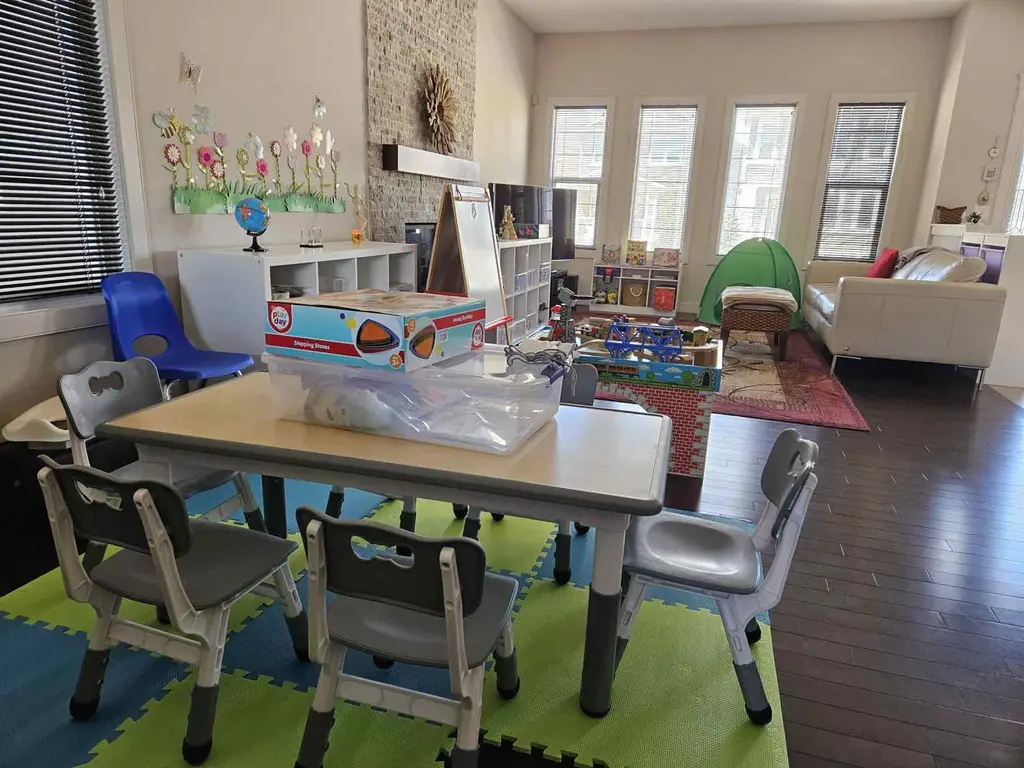 Sunny activity table with kid-sized chairs at Little Steps with Smita, with the reading tent and train table by the windows behind it
