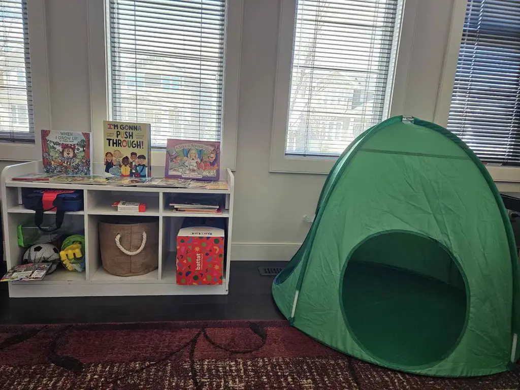 Cozy reading nook with a colourful book shelf, soft toy basket, and a green pop-up tent for quiet time