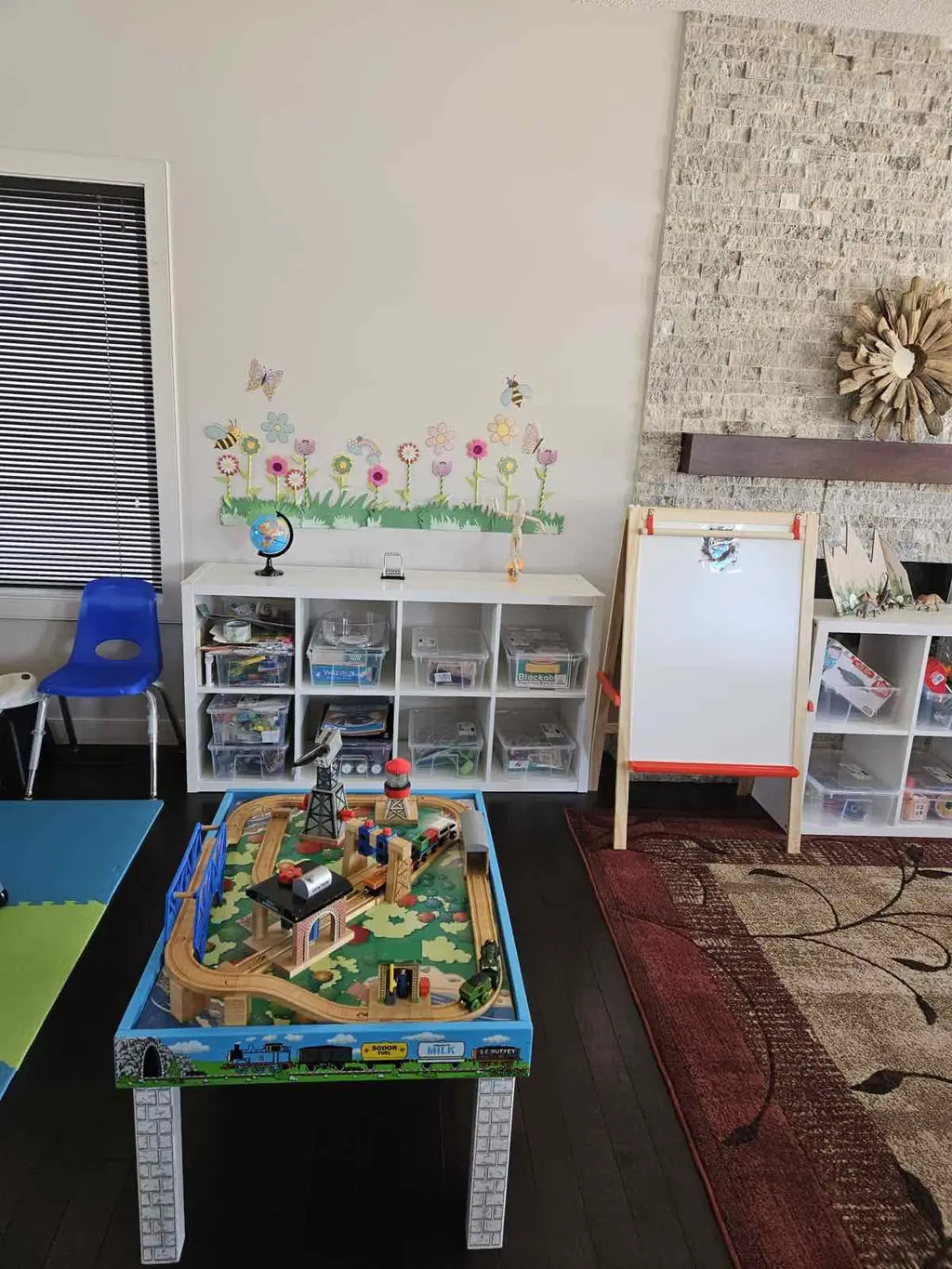 Train table play area with neatly organized toy bins, white-board easel and bright accent decals
