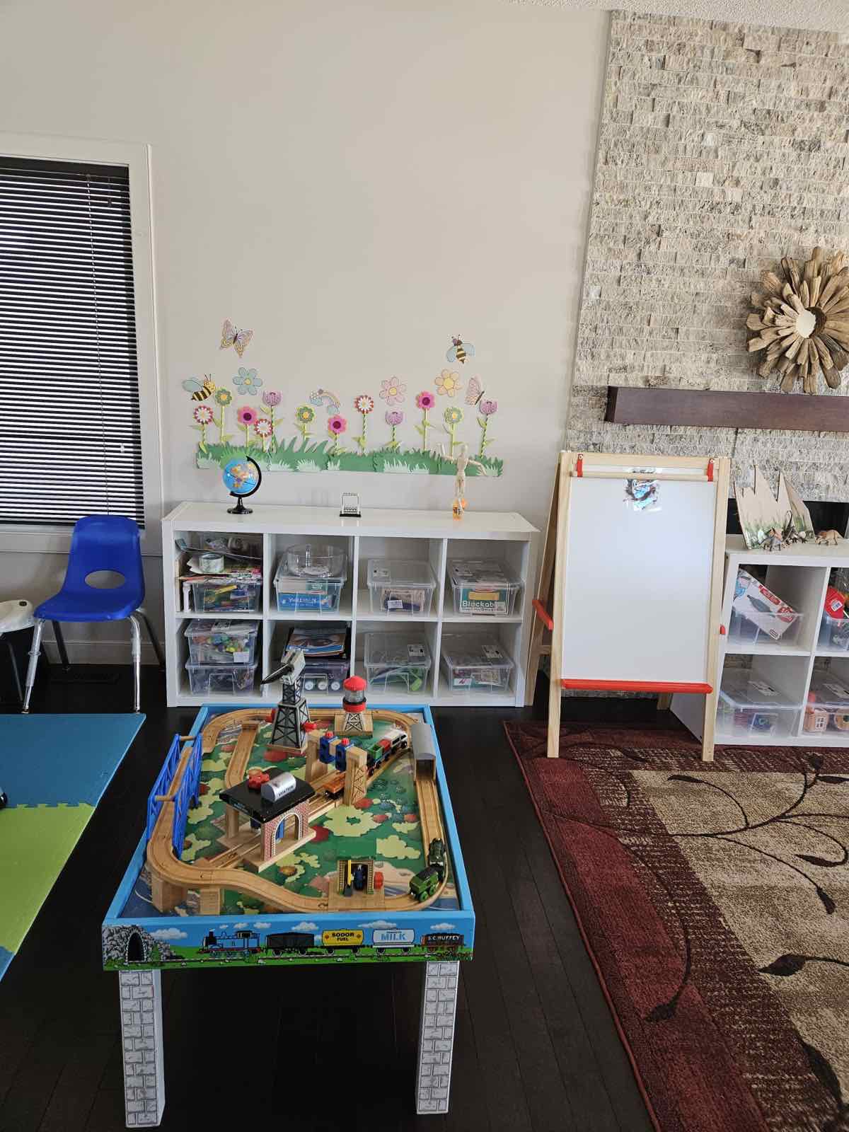 Train table play area with neatly organized toy bins, white-board easel and bright accent decals